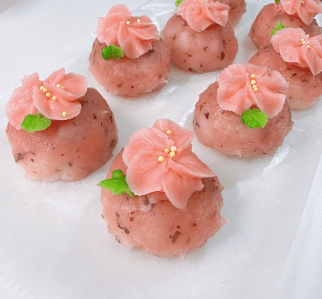 Dessert garnished with pink flower decorations made from sweet paste, served on a white background.